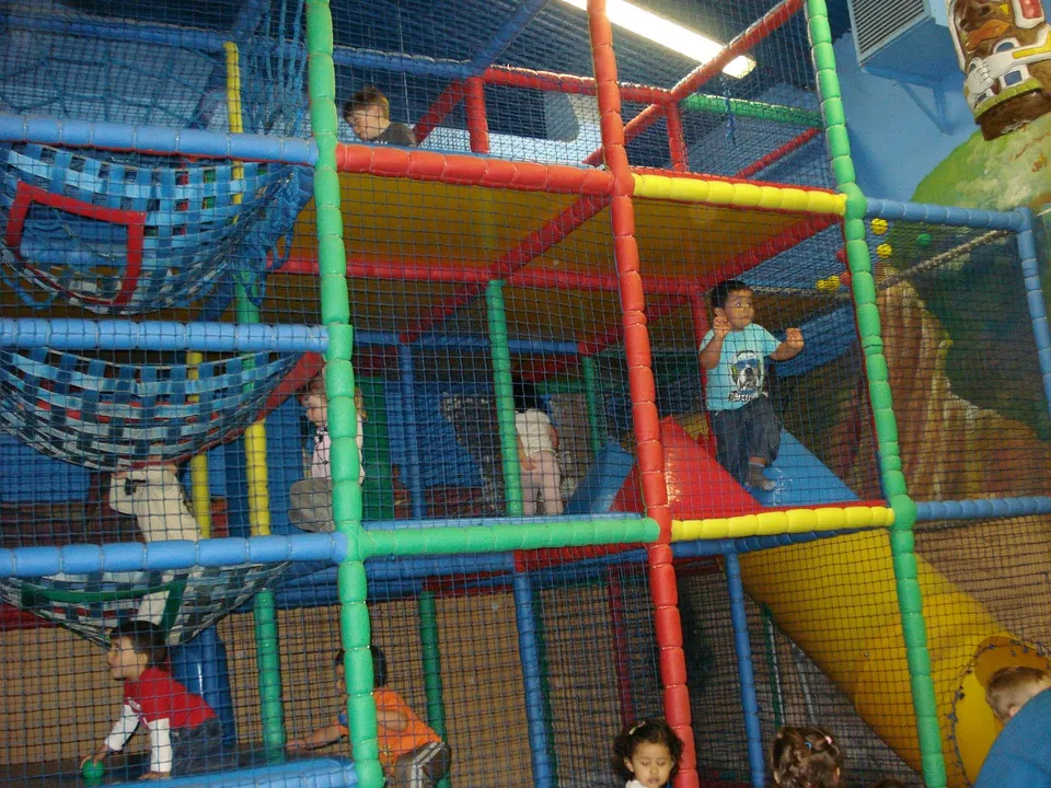 Niños jugando entre redes, tubos de colores y un tobogán en un parque infantil cubierto
